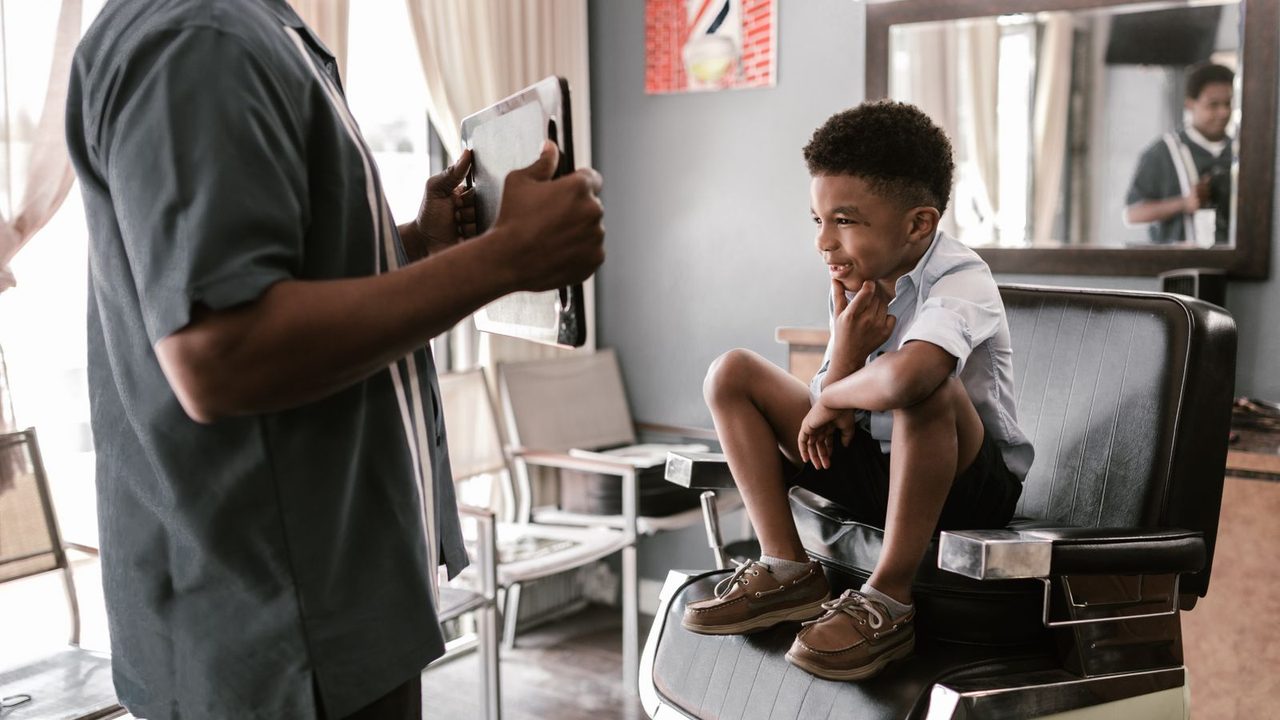 A young boy sitting in a barber chair getting his hair trimmed